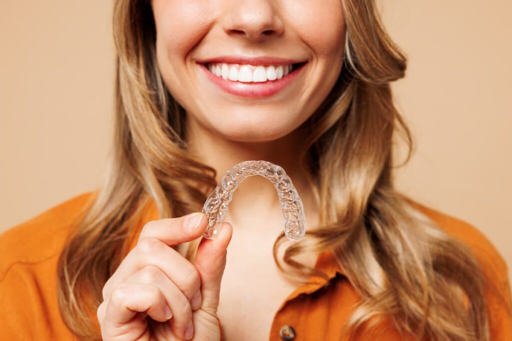 Woman smiling whilst holding Invisalign dental aligners